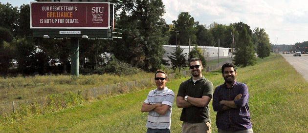 Debate team standing in front of debate billboard
